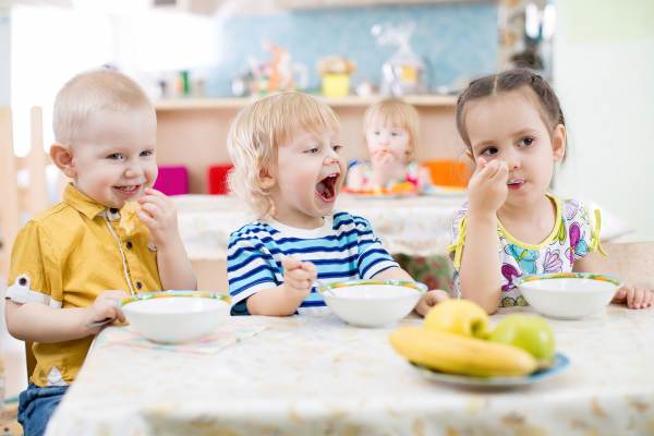 drei kleine Kinder sitzen am Tisch und essen Müsli